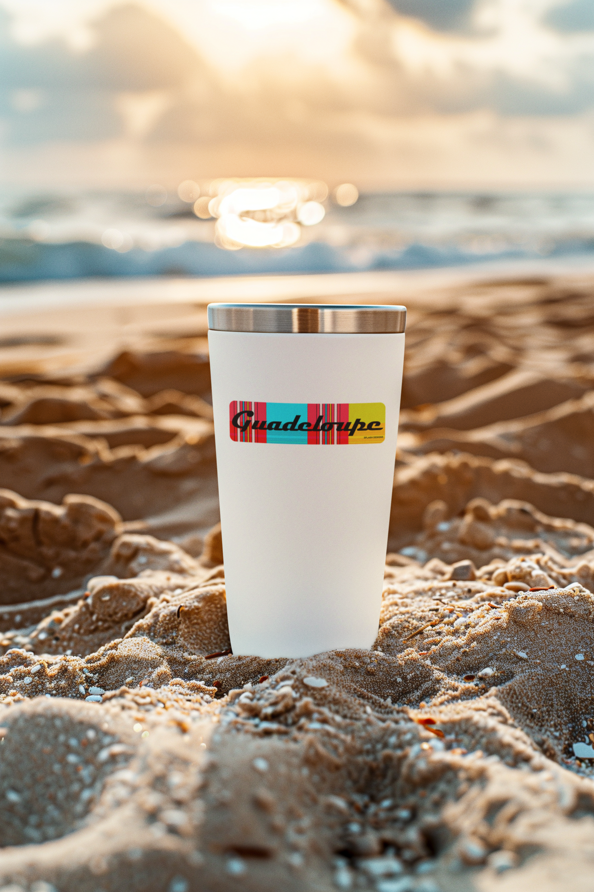 Autocollant "Guadeloupe" en papier avec motif madras "Plage des Caraïbes" de Prodigi, posé sur le sable à la plage.