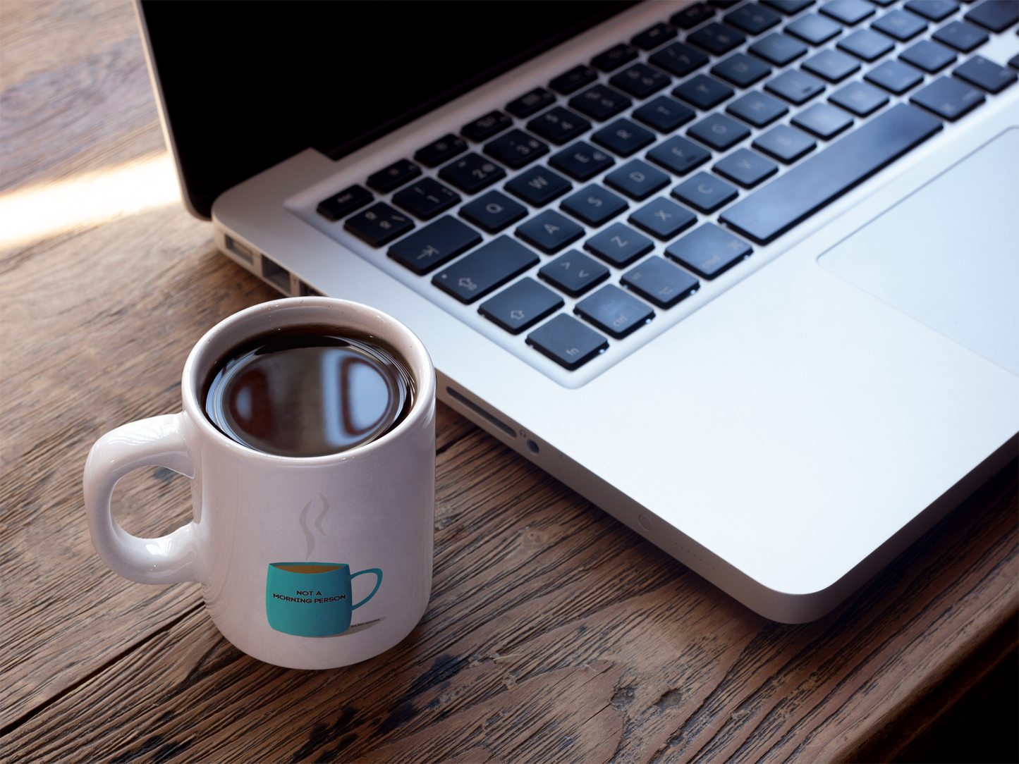 Autocollant pour mug de café "Not a morning person" de Prodigi, montrant un mug avec ce message près d'un MacBook.