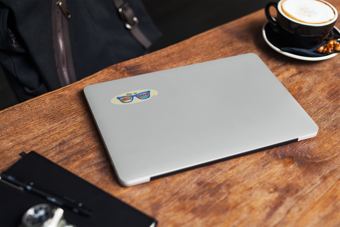 Autocollant pour lunettes "Still on Holidays" de Prodigi, couleur bleue, affiché sur un ordinateur portable sur une table en bois.