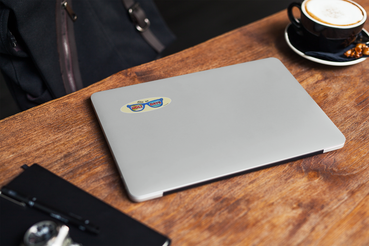 Autocollant pour lunettes "Still on Holidays" de Prodigi, couleur bleue, affiché sur un ordinateur portable sur une table en bois.