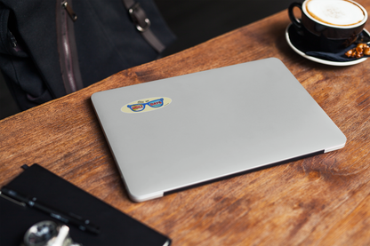 Autocollant pour lunettes "Still on Holidays" de Prodigi, couleur bleue, affiché sur un ordinateur portable sur une table en bois.
