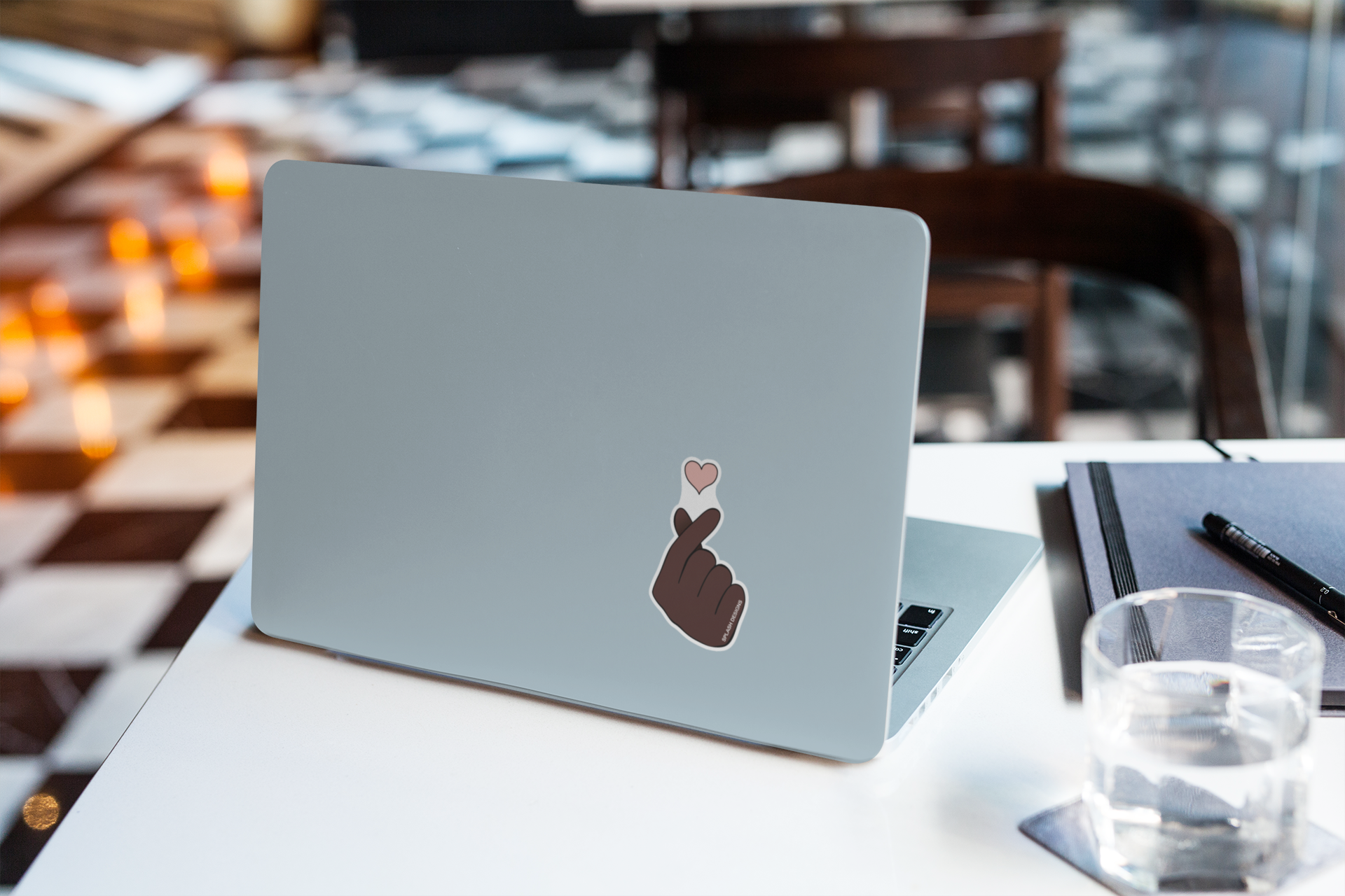 Autocollant cœur de doigt de la marque Prodigi appliqué sur une couverture d'ordinateur portable, posé à côté d'un verre d'eau.