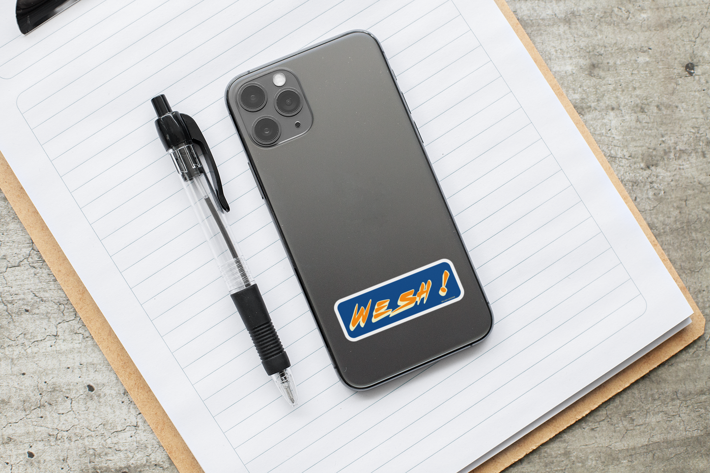 Autocollant "Wesh!" de Prodigi, sticker coloré affiché sur un téléphone avec des fournitures de bureau.