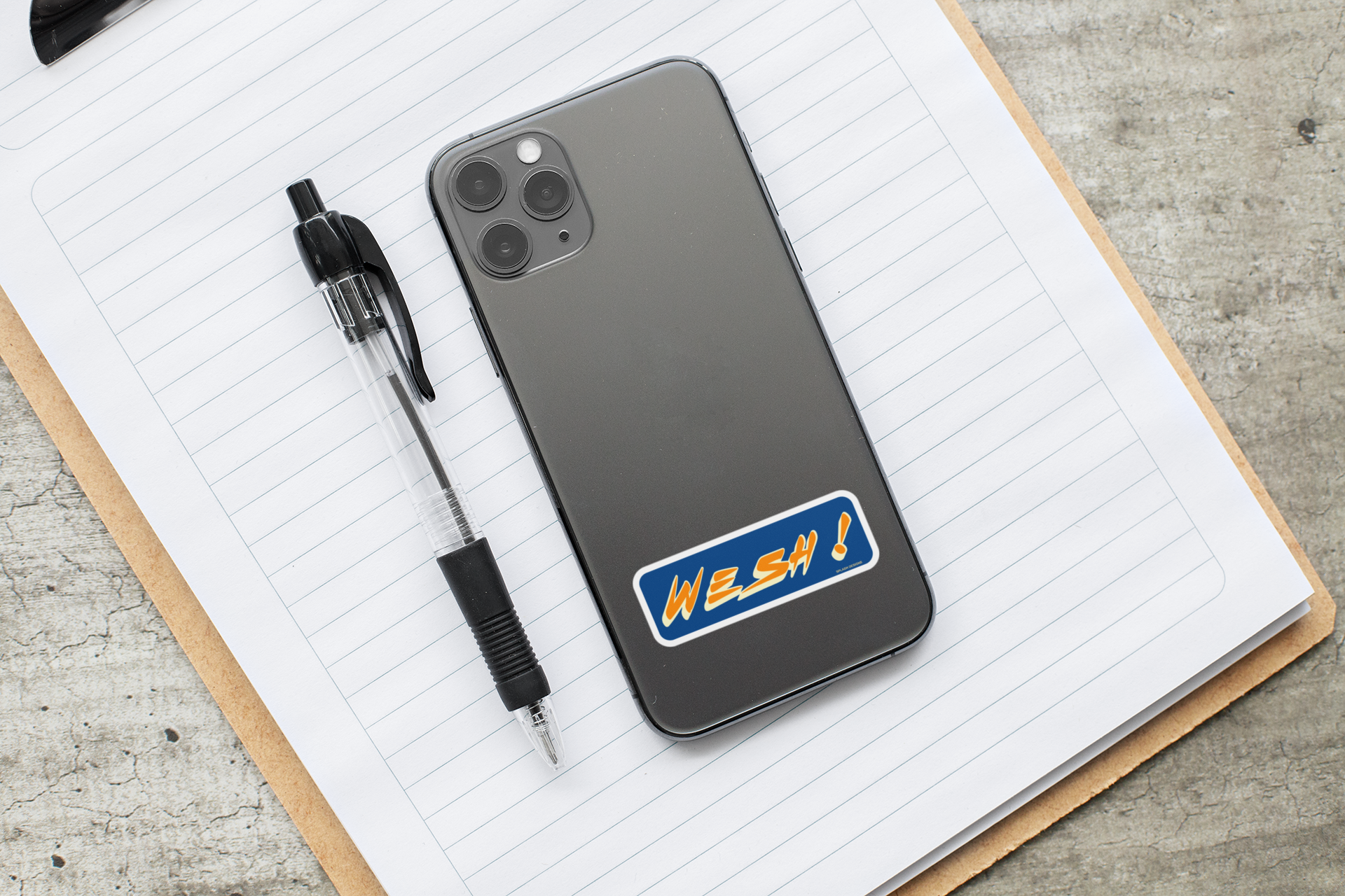 Autocollant "Wesh!" de Prodigi, sticker coloré affiché sur un téléphone avec des fournitures de bureau.